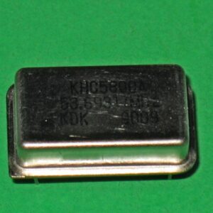 A small 230-5050 60 MHz crystal on a green surface.
