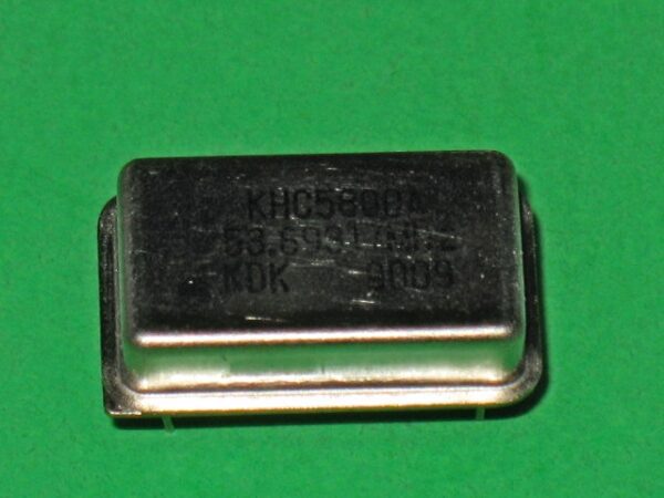 A small 230-5050 60 MHz crystal on a green surface.