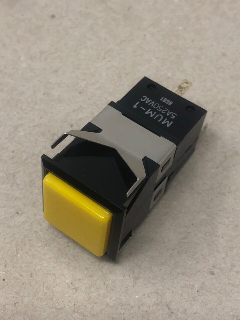 A black and yellow Square push Button on a surface.