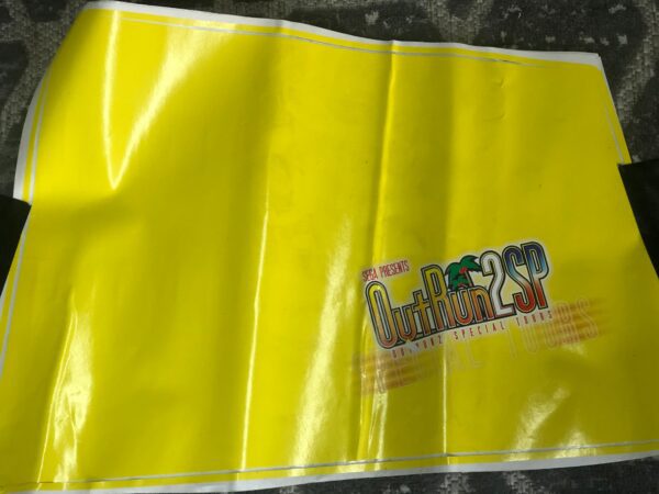 A yellow plastic bag with a black Decal, Front Right Side, Out Run 2 SP logo on it.