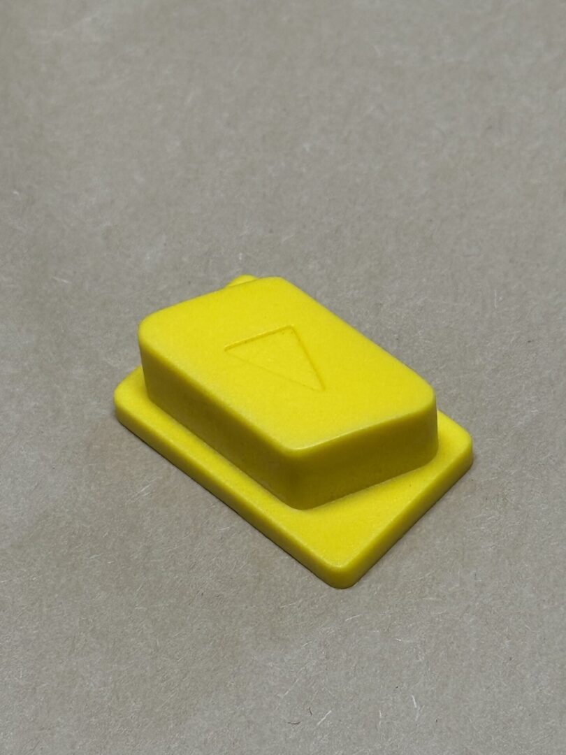 A small yellow plastic object with a raised arrow symbol.